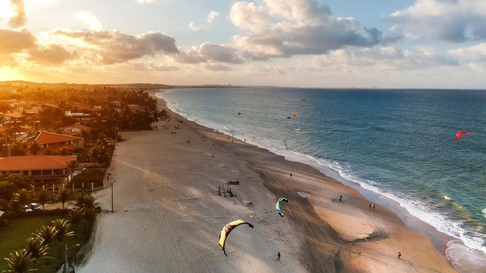 Fotografia real da orla de Cumbuco, no Ceará, com praia e kitesurf